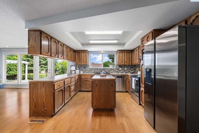 2714 W John Day Ave, Kennewick, WA 99336 - kitchen with stainless steel appliances, a peninsula, a tray ceiling, light wood finished floors, and a textured ceiling
