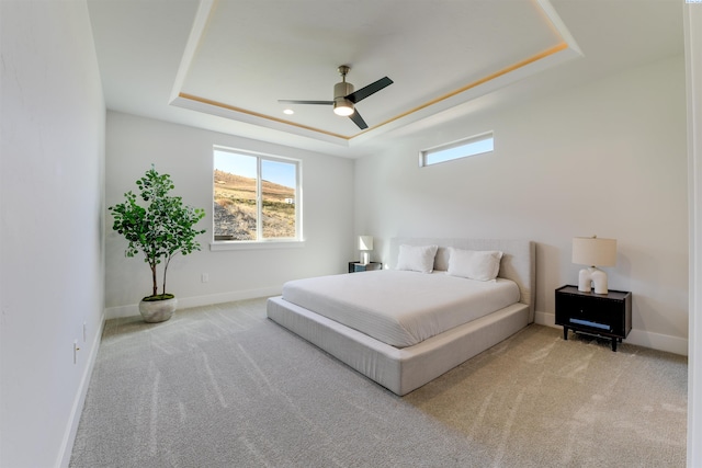 carpeted bedroom with ceiling fan and a tray ceiling