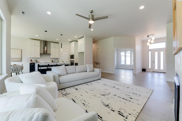 living room featuring ceiling fan with notable chandelier and light hardwood / wood-style floors