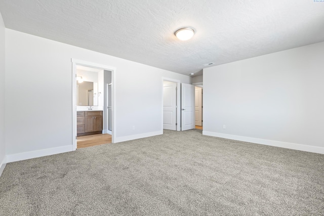 unfurnished bedroom featuring light carpet, baseboards, a textured ceiling, and ensuite bathroom