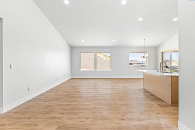 unfurnished living room with a chandelier, a sink, a textured ceiling, healthy amount of natural light, and recessed lighting