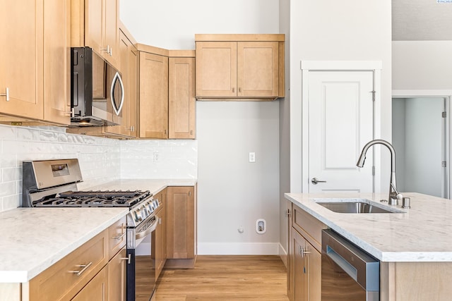 kitchen featuring appliances with stainless steel finishes, a sink, baseboards, light wood-type flooring, and tasteful backsplash
