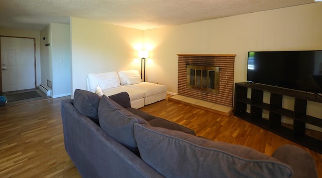 living room with hardwood / wood-style flooring, a brick fireplace, and a textured ceiling