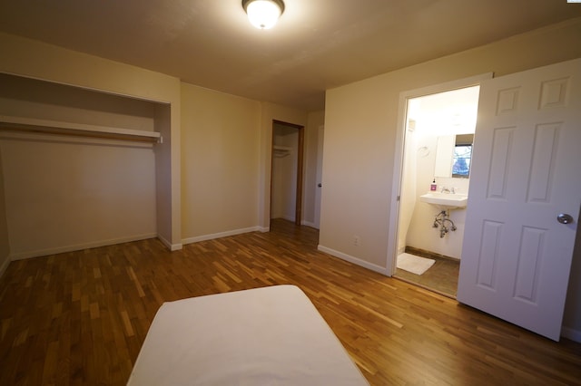 unfurnished bedroom featuring hardwood / wood-style flooring, ensuite bath, and multiple closets