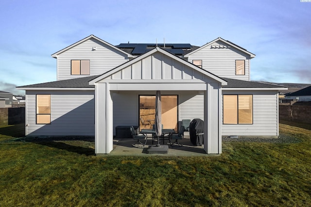 back of house with roof with shingles, a lawn, board and batten siding, a patio area, and fence