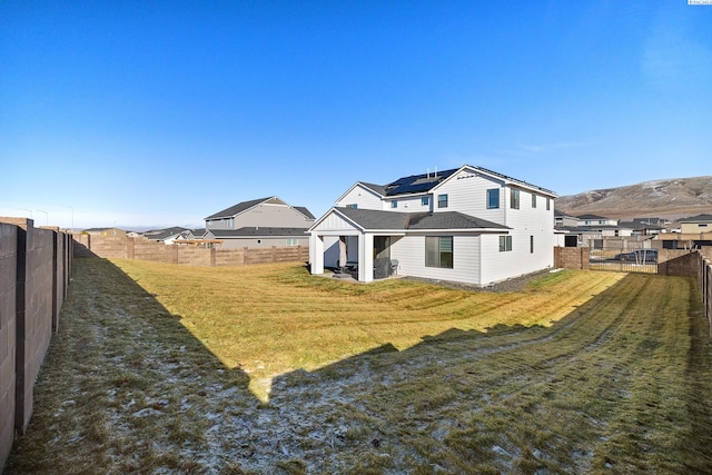 rear view of property featuring a fenced backyard, a residential view, a lawn, and roof mounted solar panels