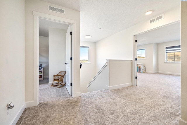 hall with baseboards, visible vents, light carpet, and an upstairs landing