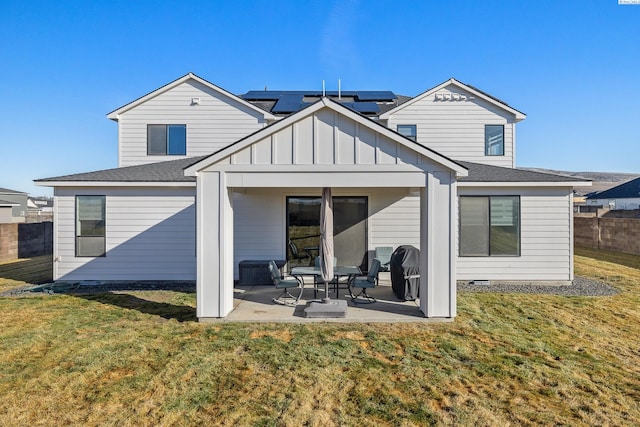 rear view of house with a patio, a lawn, board and batten siding, roof mounted solar panels, and fence