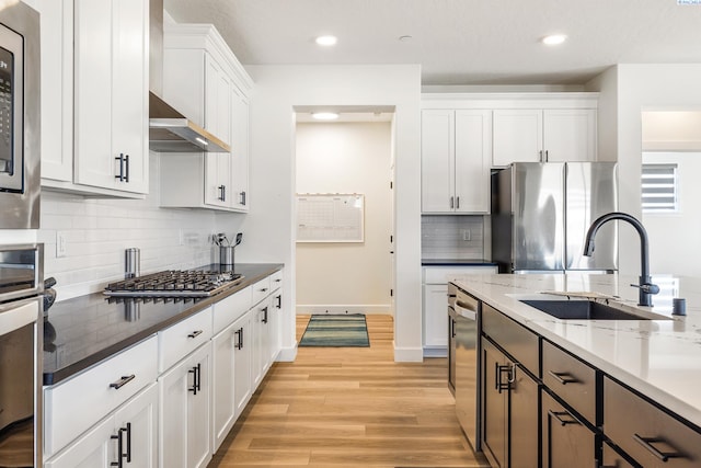 kitchen featuring light stone counters, stainless steel appliances, light wood-style flooring, white cabinets, and a sink