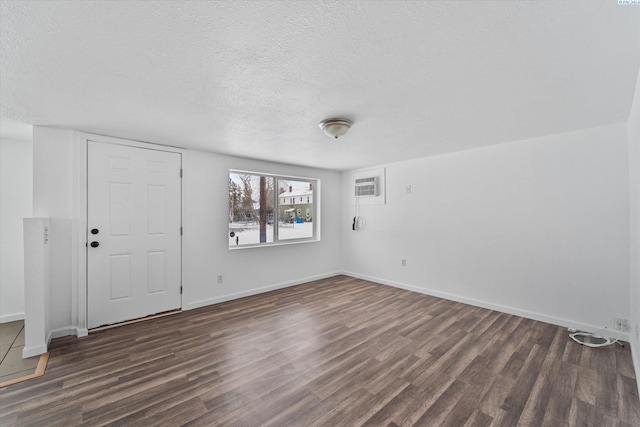 spare room featuring dark wood-type flooring, an AC wall unit, and a textured ceiling