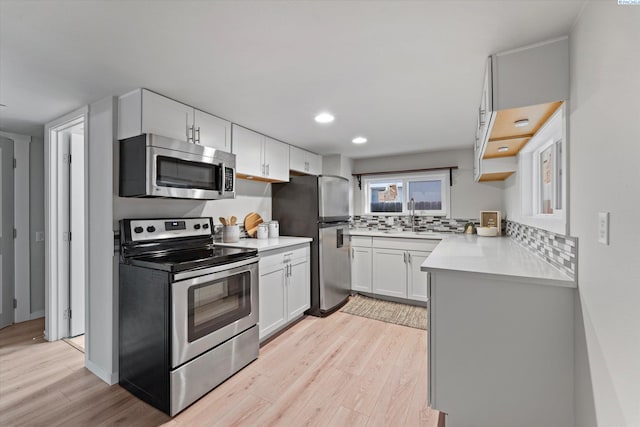 kitchen featuring tasteful backsplash, light countertops, appliances with stainless steel finishes, a sink, and light wood-type flooring