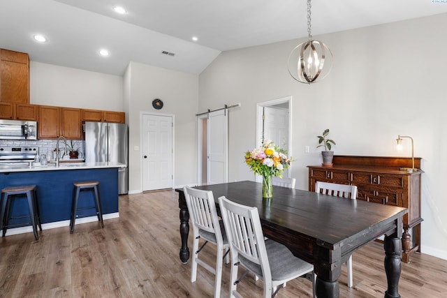 1707 W 25th Pl, Kennewick, WA 99337 - dining area featuring a barn door, light wood-style floors, high vaulted ceiling, a chandelier, and baseboards