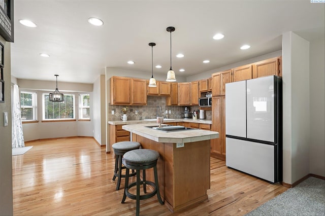 2302 W 31st Ave, Kennewick, WA 99337 - kitchen with freestanding refrigerator, a kitchen island with sink, baseboards, light wood finished floors, and backsplash