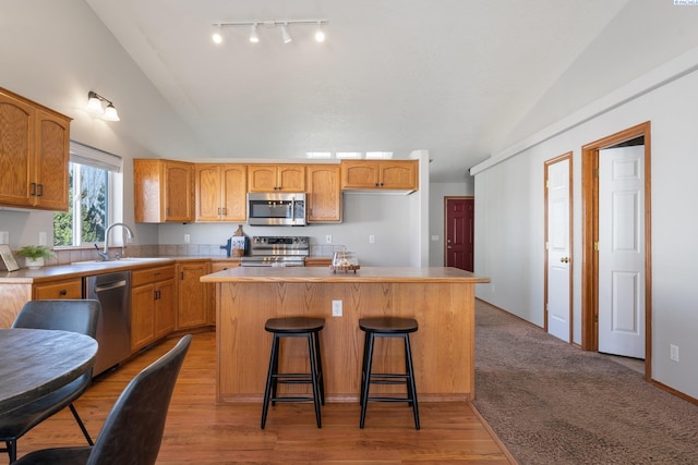 kitchen featuring a center island, stainless steel appliances, lofted ceiling, light countertops, and a sink