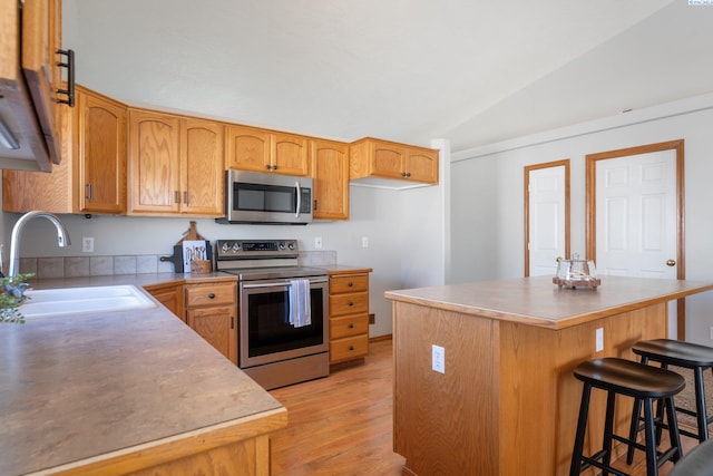 kitchen with a center island, appliances with stainless steel finishes, vaulted ceiling, a sink, and a kitchen breakfast bar