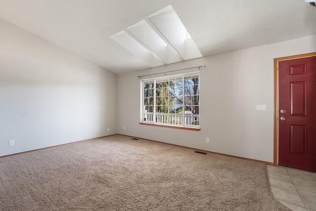 spare room featuring vaulted ceiling with skylight, light tile patterned flooring, light colored carpet, visible vents, and baseboards