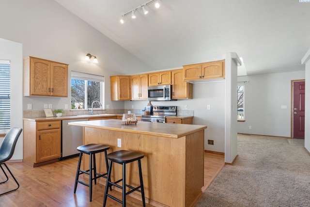 kitchen with high vaulted ceiling, a breakfast bar area, a sink, appliances with stainless steel finishes, and a center island