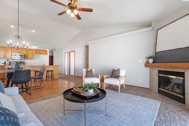 living area featuring a tile fireplace, vaulted ceiling, baseboards, and ceiling fan with notable chandelier