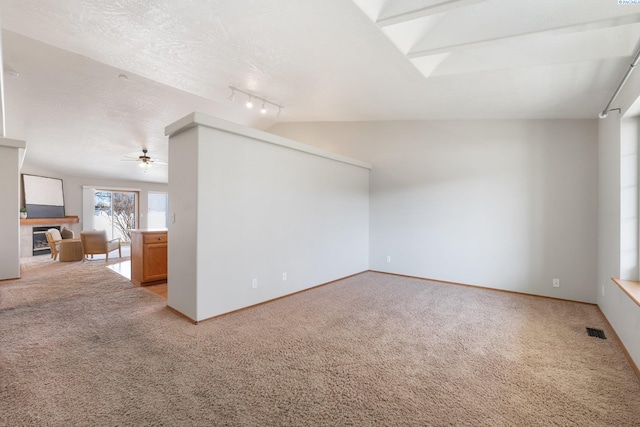 empty room featuring vaulted ceiling, a fireplace, visible vents, and light colored carpet