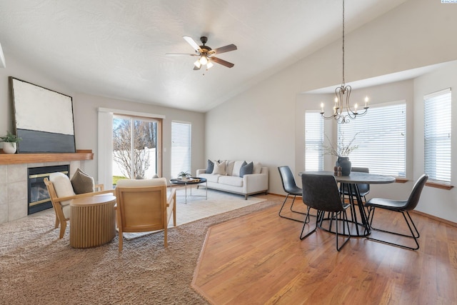 dining room featuring lofted ceiling, a tile fireplace, ceiling fan with notable chandelier, wood finished floors, and baseboards