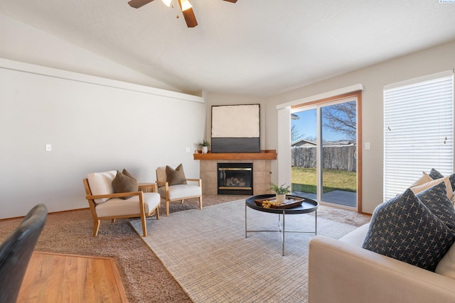 living room with vaulted ceiling, ceiling fan, a tiled fireplace, and wood finished floors