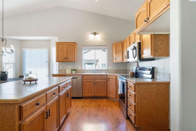 kitchen with appliances with stainless steel finishes, light countertops, light wood-type flooring, pendant lighting, and a sink