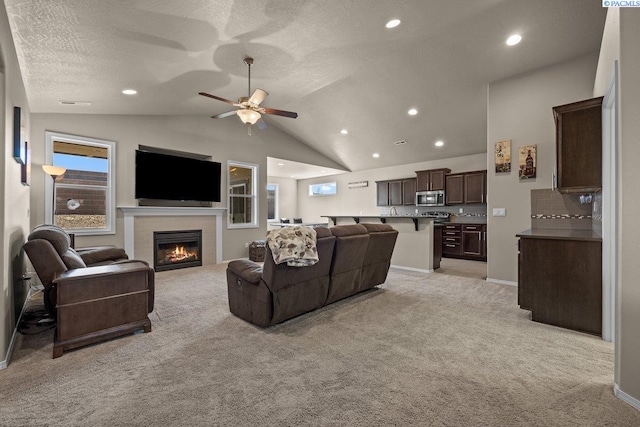 living area featuring a fireplace, lofted ceiling, light carpet, ceiling fan, and a textured ceiling