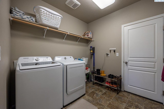 laundry area with laundry area, visible vents, stone finish flooring, and washing machine and clothes dryer