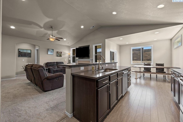 kitchen with dark brown cabinetry, dark countertops, lofted ceiling, open floor plan, and a sink