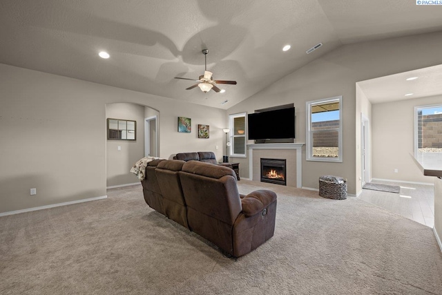 living area with ceiling fan, carpet floors, baseboards, vaulted ceiling, and a lit fireplace