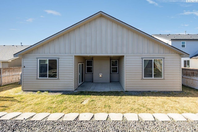 rear view of house featuring board and batten siding, a patio area, fence, and a lawn