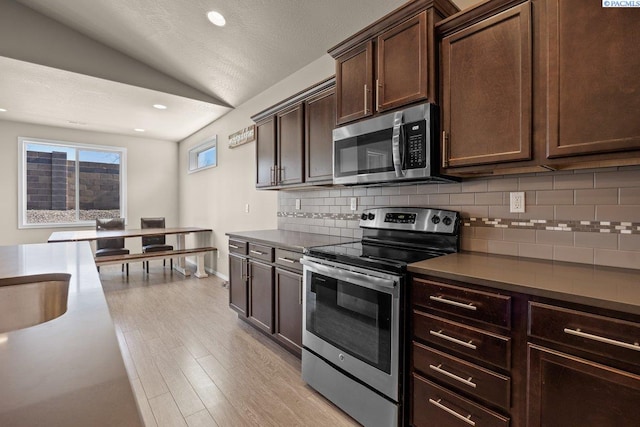 kitchen featuring tasteful backsplash, lofted ceiling, appliances with stainless steel finishes, light wood-style floors, and dark brown cabinetry