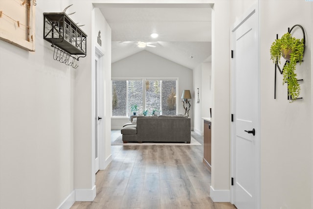 hall featuring vaulted ceiling, light wood-type flooring, and baseboards