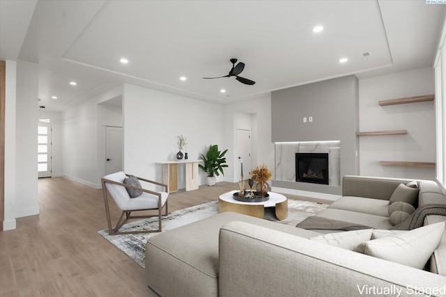 living room with a high end fireplace, light hardwood / wood-style flooring, and ceiling fan