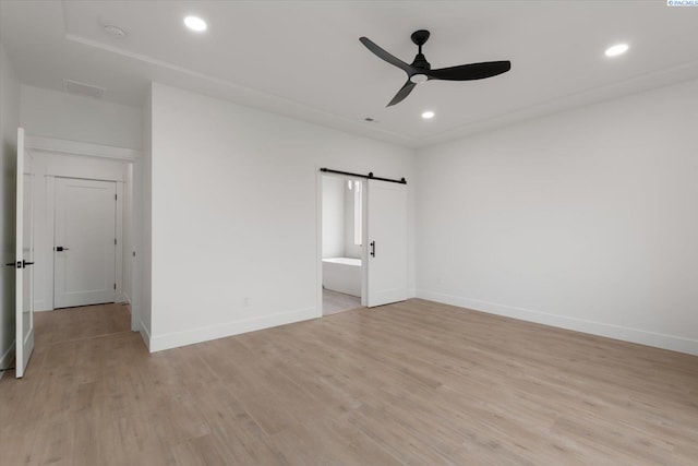 unfurnished bedroom featuring light hardwood / wood-style floors, a barn door, and ceiling fan