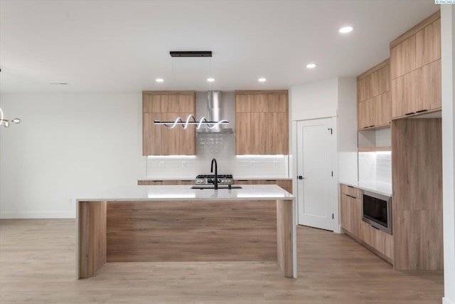 kitchen with hanging light fixtures, tasteful backsplash, a kitchen island with sink, and light brown cabinets