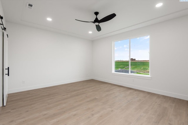 unfurnished room featuring light hardwood / wood-style flooring, a barn door, and ceiling fan