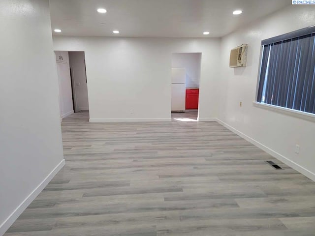 spare room featuring a wall unit AC, light wood-type flooring, baseboards, and recessed lighting