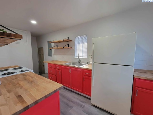 kitchen featuring butcher block countertops, a sink, red cabinets, freestanding refrigerator, and tasteful backsplash