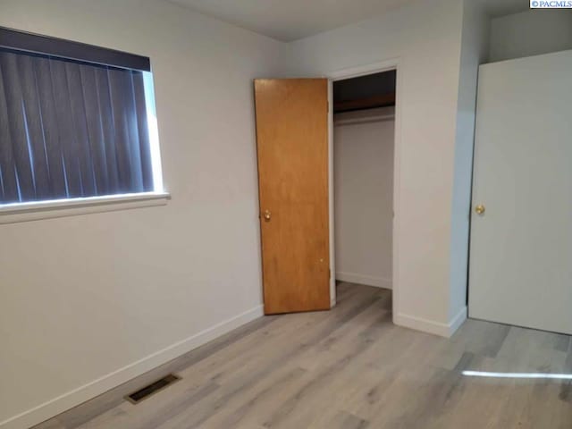 unfurnished bedroom with baseboards, a closet, visible vents, and wood finished floors