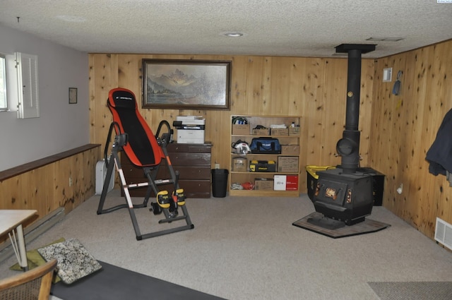 workout area with carpet, a wood stove, wood walls, and a textured ceiling