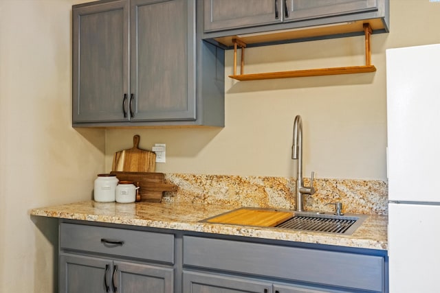 kitchen with gray cabinetry, sink, light stone countertops, and white fridge