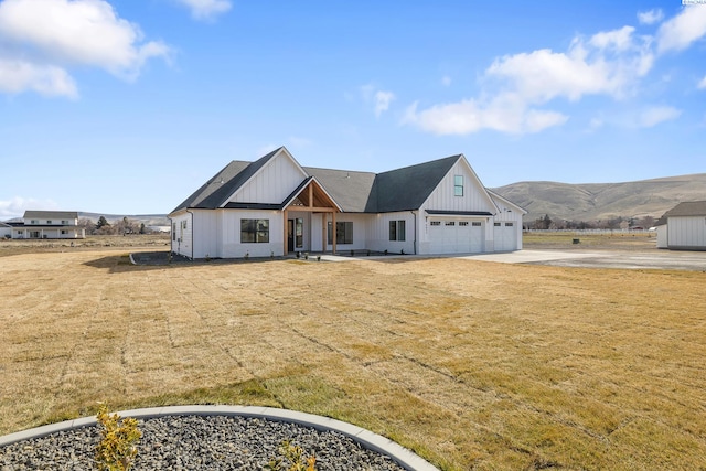 modern farmhouse featuring board and batten siding, a mountain view, a garage, driveway, and a front lawn