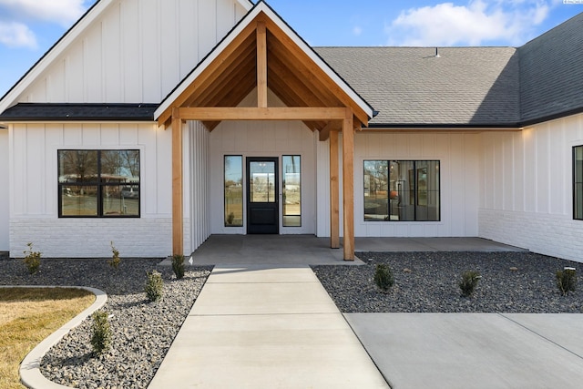 property entrance with board and batten siding, roof with shingles, and brick siding