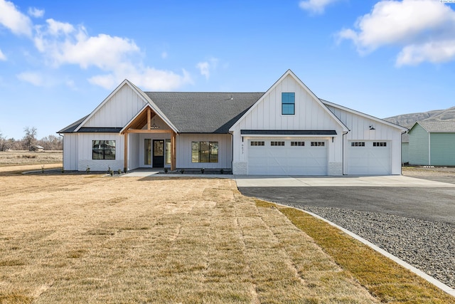 modern farmhouse featuring brick siding, roof with shingles, board and batten siding, a front yard, and driveway