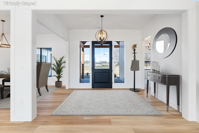 entryway featuring baseboards, a healthy amount of sunlight, light wood-type flooring, and an inviting chandelier