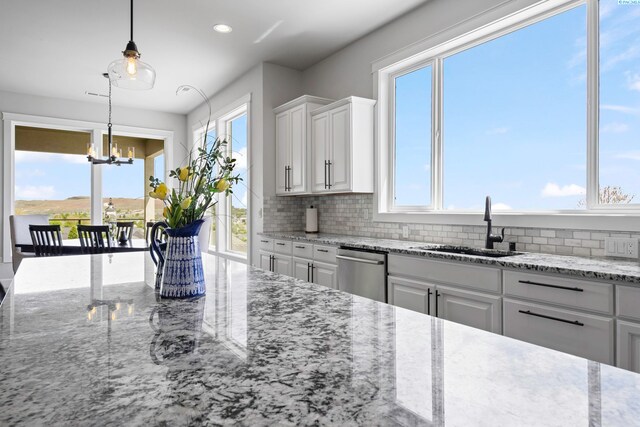 kitchen featuring white cabinetry, sink, hanging light fixtures, stainless steel dishwasher, and light stone countertops