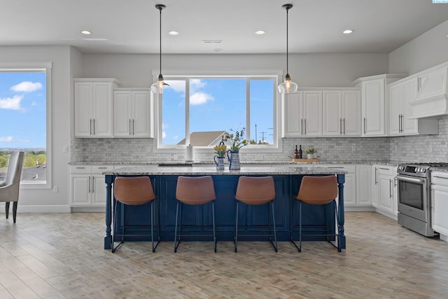 kitchen featuring white cabinetry, stainless steel range, light stone countertops, and a kitchen island