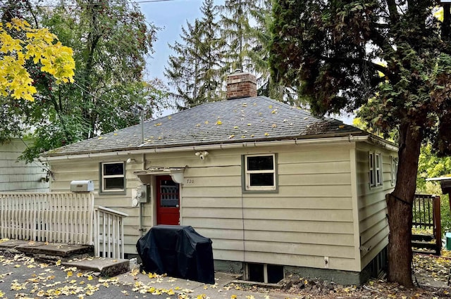 rear view of house featuring roof with shingles, fence, and a chimney