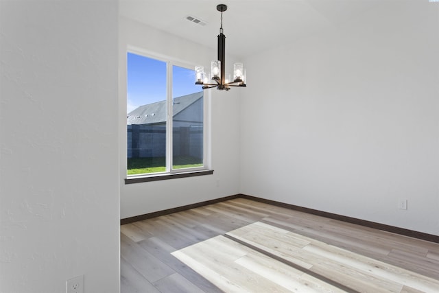 unfurnished dining area featuring an inviting chandelier and light hardwood / wood-style floors